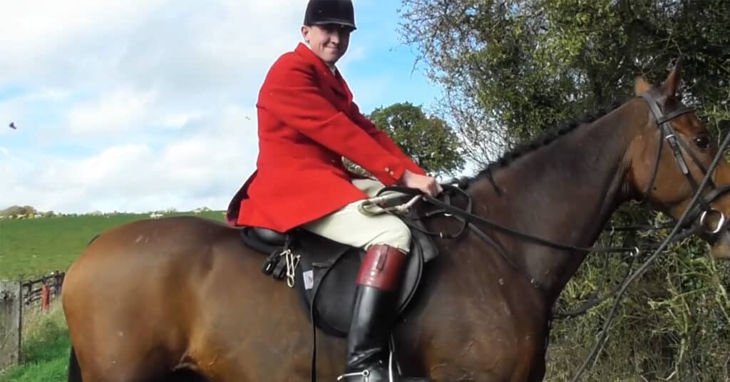 Whipper-in Hartley Crouch looks directly into the camera, held by a sab with Hertfordshire Hunt Saboteurs